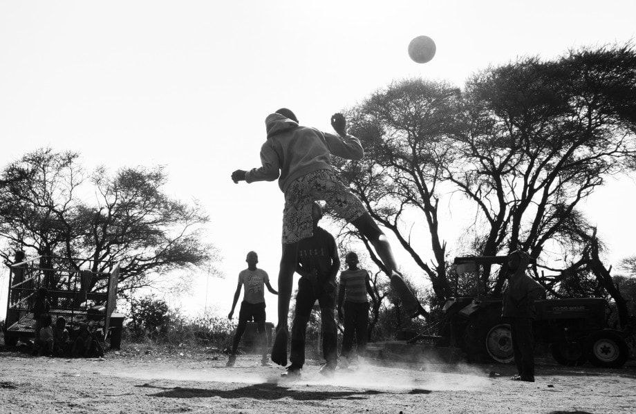 young children play football in the dust next to a farmer’s tractor in mpumalanga.